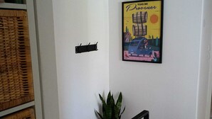 A hallway with a framed poster, wicker baskets, a potted plant, and a staircase with black railings. - Cosy, spacious air-conditioned apartment with all mod cons (Puget-ville)