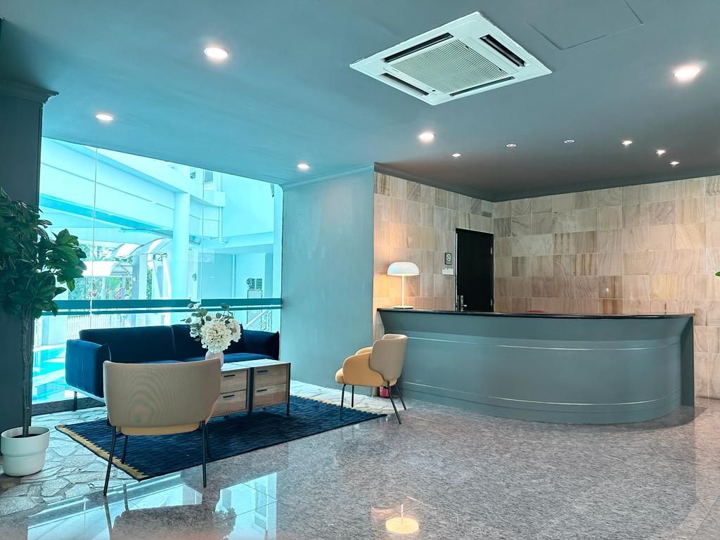 A modern reception area with a curved desk, a sofa, and a chair. There is a potted plant and a lamp.