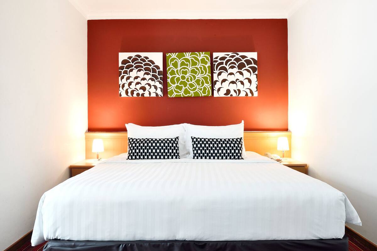 A hotel room with a large bed, two bedside tables with lamps, and three wall art pieces above the bed.