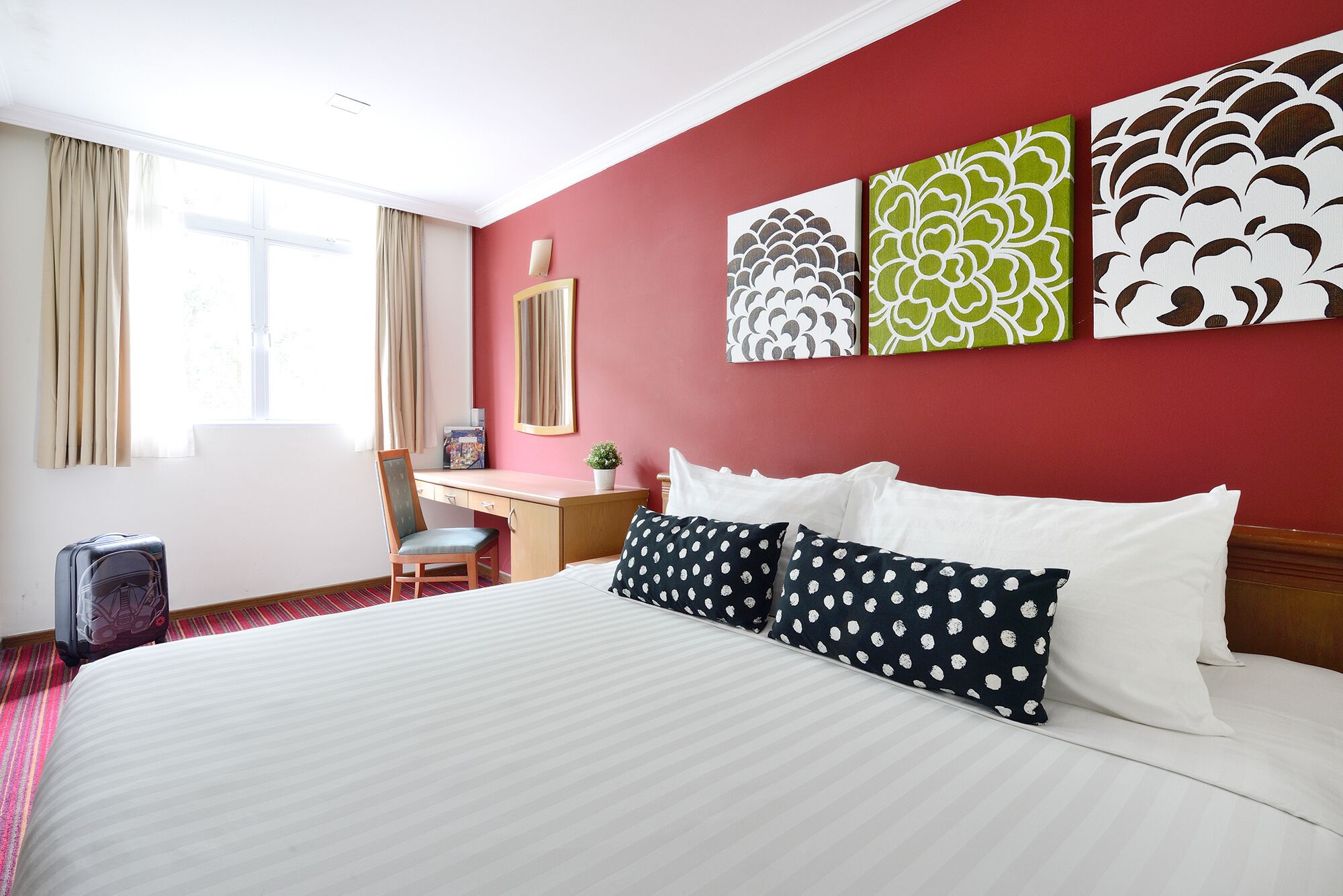 A hotel room with a bed, a desk, a chair, and artwork on the wall.