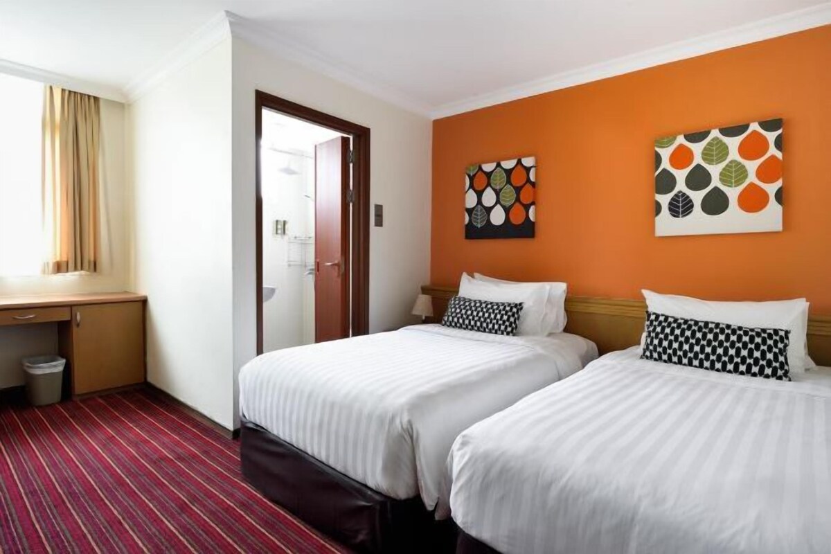 A hotel room with two beds, a desk, and a window.