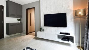 Una sala de estar moderna con un televisor de pantalla plana montado en una pared de mármol, un mueble blanco de entretenimiento debajo y una lámpara de pie a la derecha.