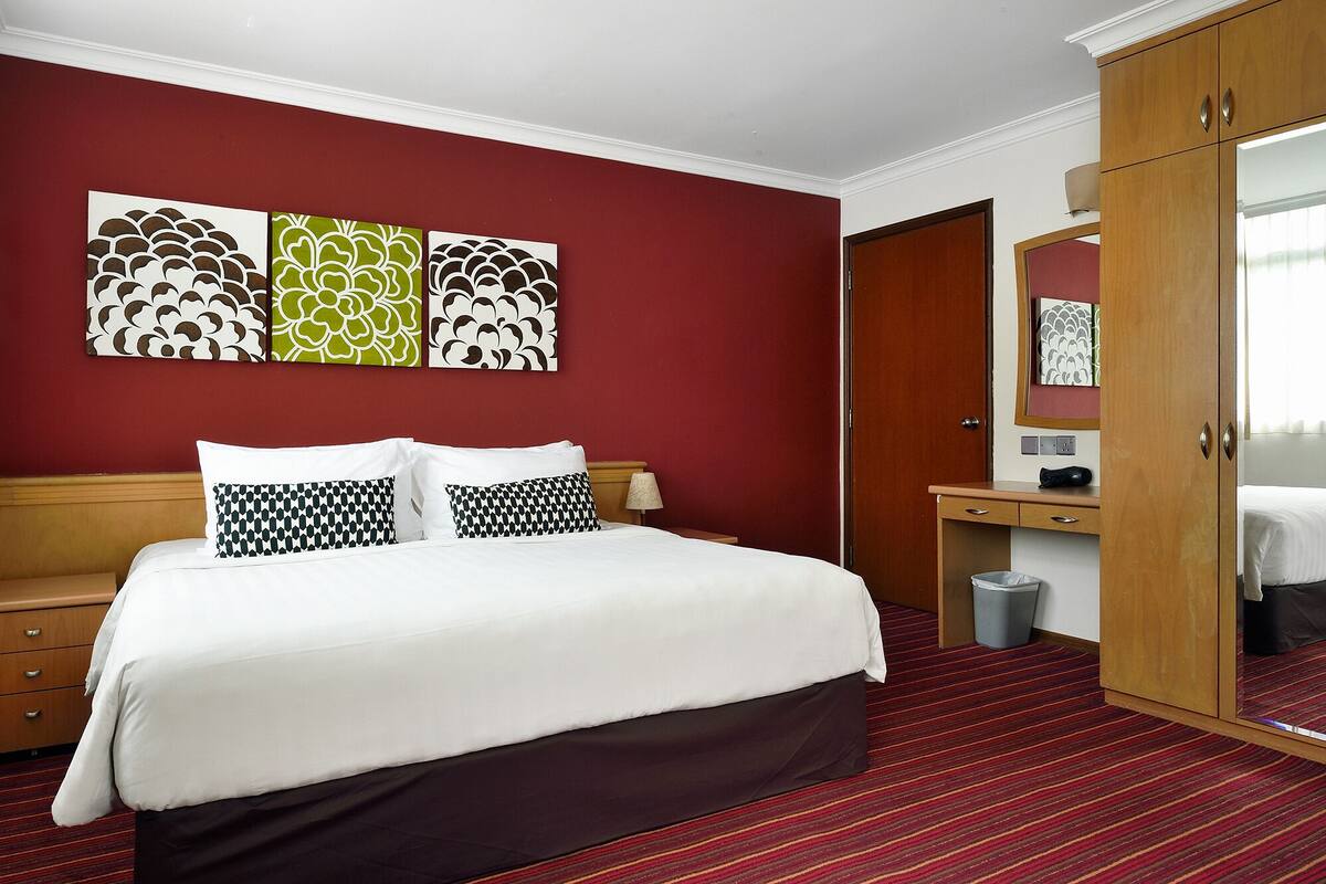A hotel room with a bed, a nightstand, a dresser, a mirror, and a red carpeted floor.