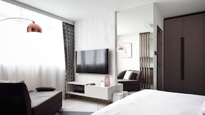 Una habitación de hotel moderna con una cama grande, un sofá, un televisor montado en la pared y un escritorio con una lámpara.
