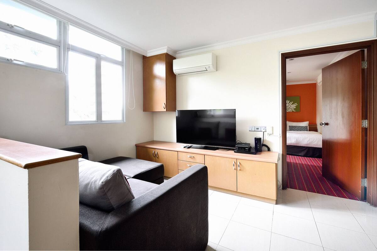 A hotel room with a TV, a desk, a chair, a bed, and a door leading to another room.