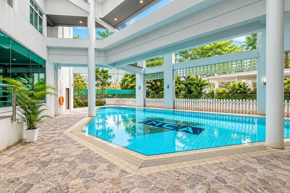 A swimming pool with a tiled deck, surrounded by a white fence and greenery.