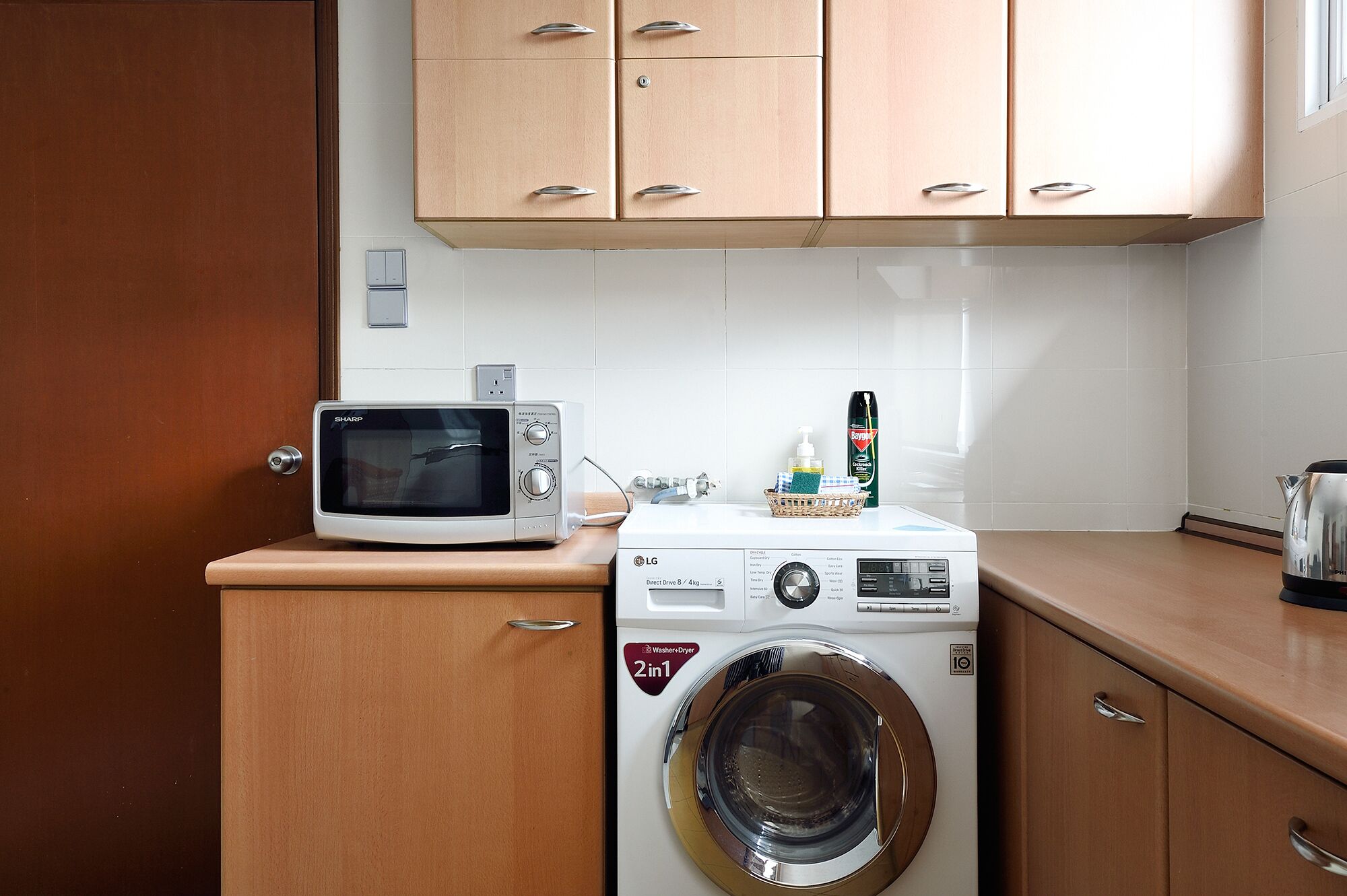 A compact kitchen with a microwave, washing machine, and a kettle.