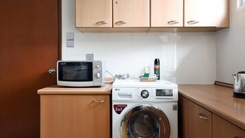 A compact kitchen with a microwave, washing machine, and a kettle.