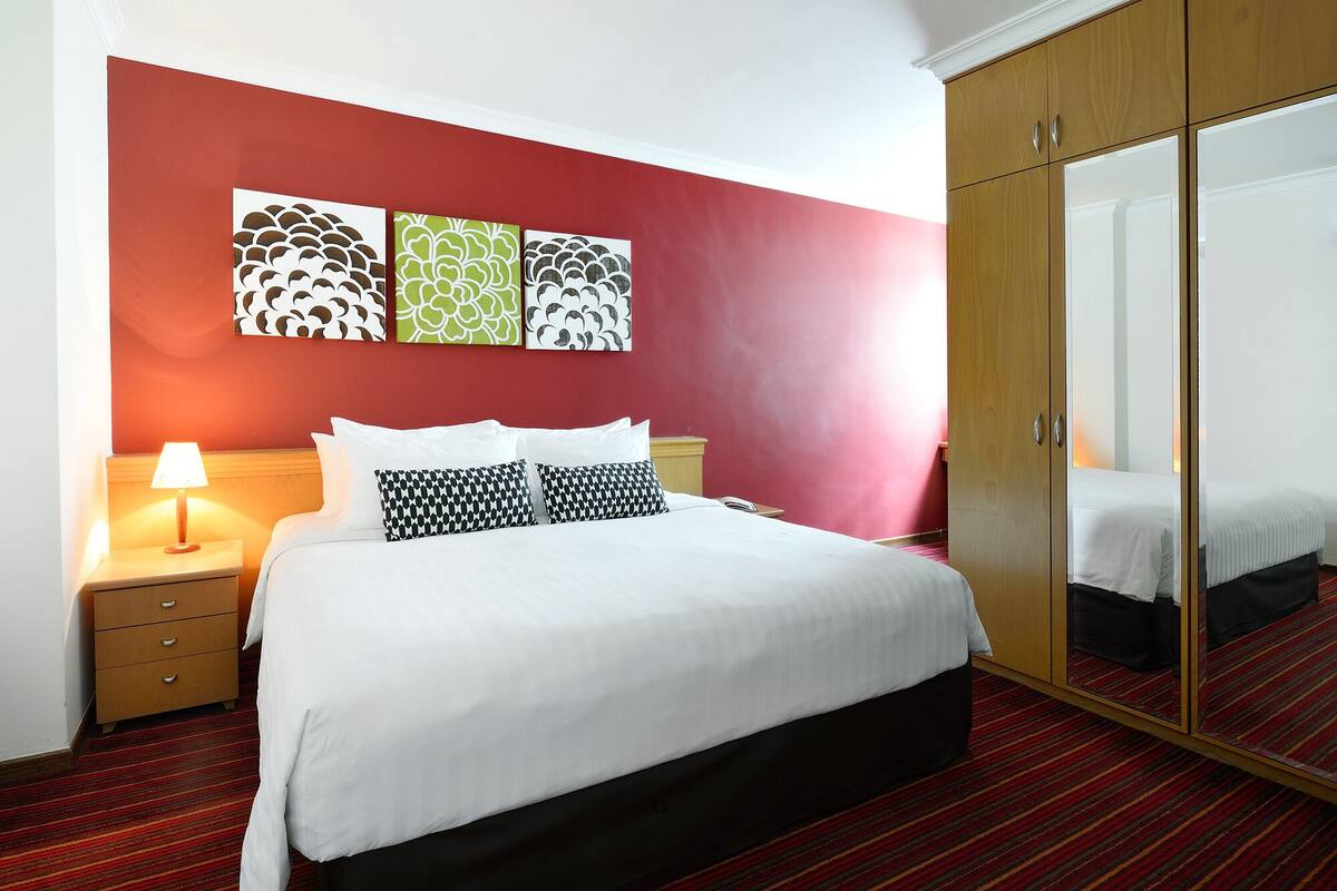 A hotel room with a bed, a nightstand, a lamp, a wardrobe, and three wall art pieces.