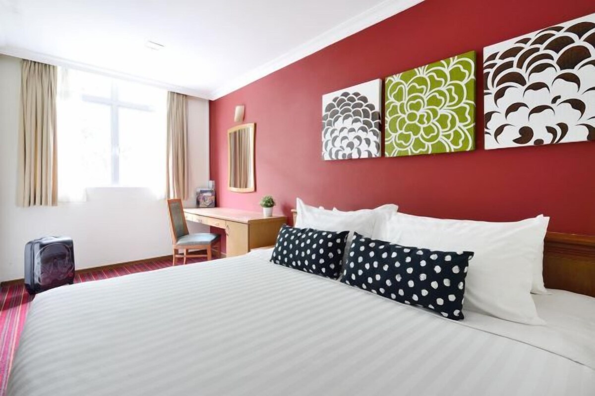 A hotel room with a large bed, a desk, a chair, and artwork on the wall.