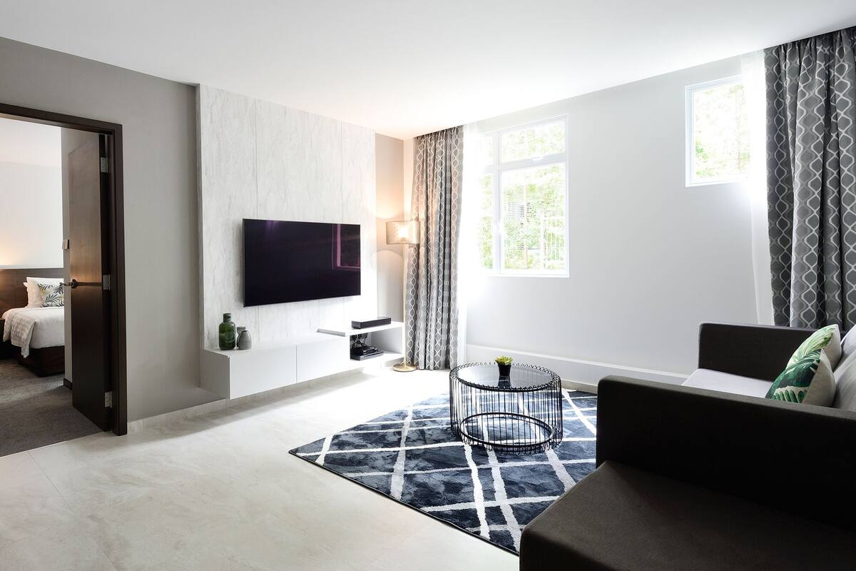 A modern living room with a flat-screen TV mounted on the wall, a sofa, a coffee table, and a patterned rug.