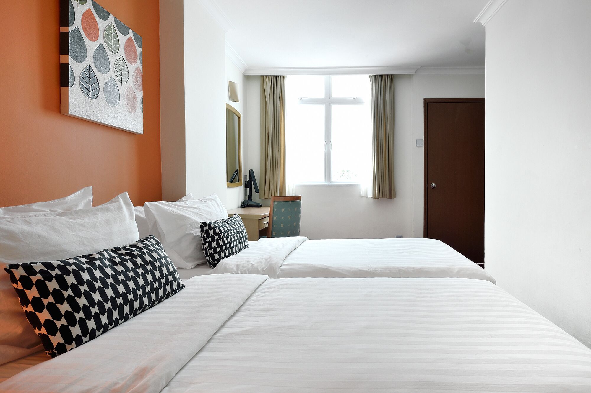 Une chambre d’hôtel avec deux lits, un bureau, une chaise, un miroir et une fenêtre avec des rideaux.