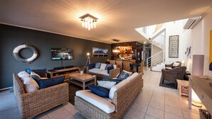 Een ruime woonkamer met rieten meubilair, een flatscreen-tv en een trap naar een verdieping.