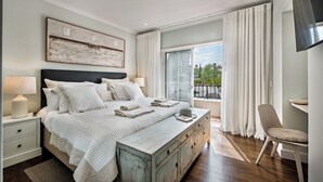Ein Schlafzimmer mit einem großen Bett, Nachttischen, einer Kommode, einem Sessel und einem Fenster mit Vorhängen.