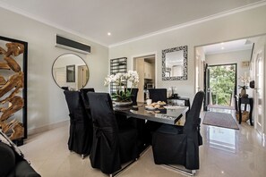 A dining area with a black table, chairs, and a vase of white flowers. There are two mirrors on the walls and a wooden sculpture on the left.