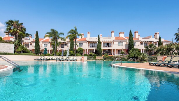 Ein Pool mit Liegestühlen und Palmen, umgeben von mehrstöckigen Gebäuden mit Balkonen.
