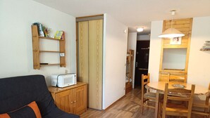Ett mysigt vardagsrum med en soffa, ett träskåp, en mikrovågsugn och ett matbord med stolar.