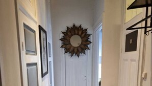 Un pasillo con suelo de madera, puertas blancas y un espejo con diseño de sol en la pared.