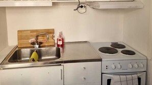 Una cocina compacta con armarios blancos, un lavamanos, una estufa y una pequeña encimera.