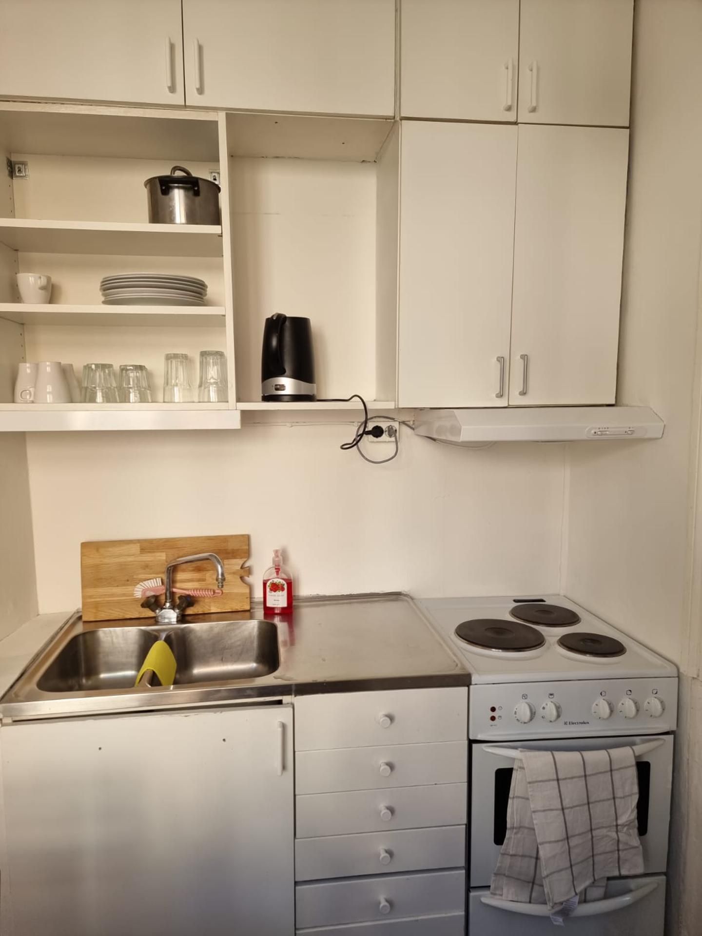 A compact kitchen with white cabinets, a stainless steel sink, a stove, and a small countertop.