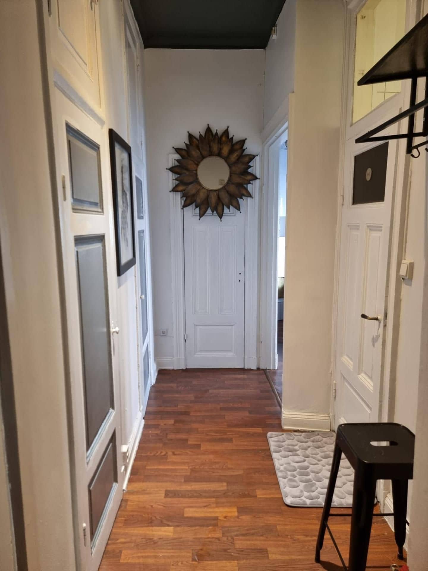 A hallway with wooden flooring, white doors, and a sunburst mirror on the wall.
