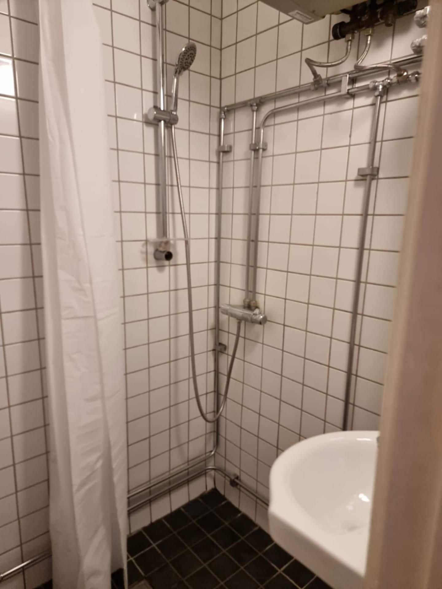 Casa de banho com paredes revestidas a azulejos brancos, chuveiro com chuveiro de mão e lavatório branco.