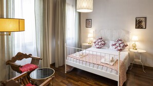 Ein Schlafzimmer mit Bett, Nachttischlampen, einem Sessel, einem Tisch und einer Pendelleuchte.