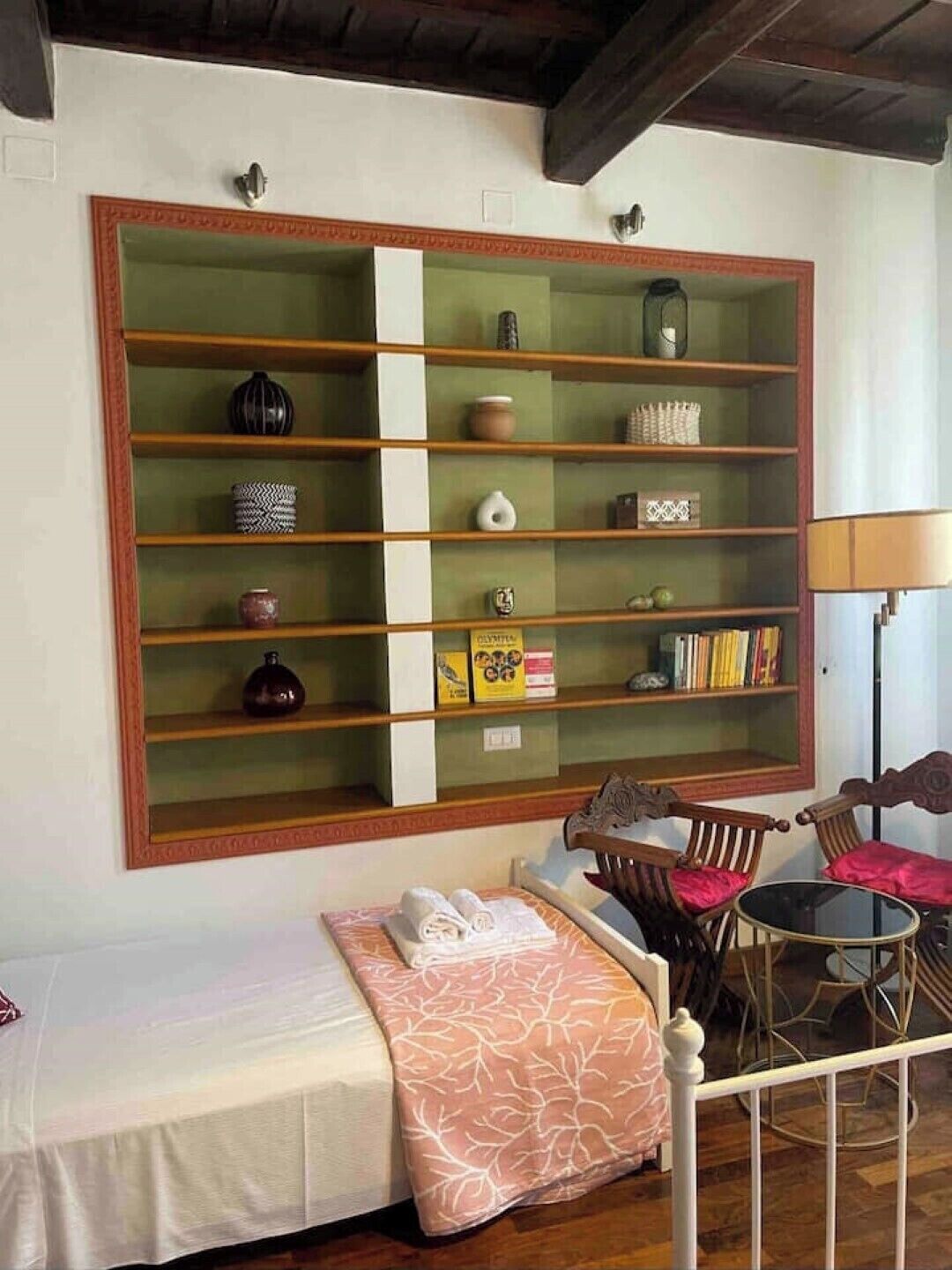A room with a large bookshelf, a bed with a pink patterned pillow, and a small table with chairs.