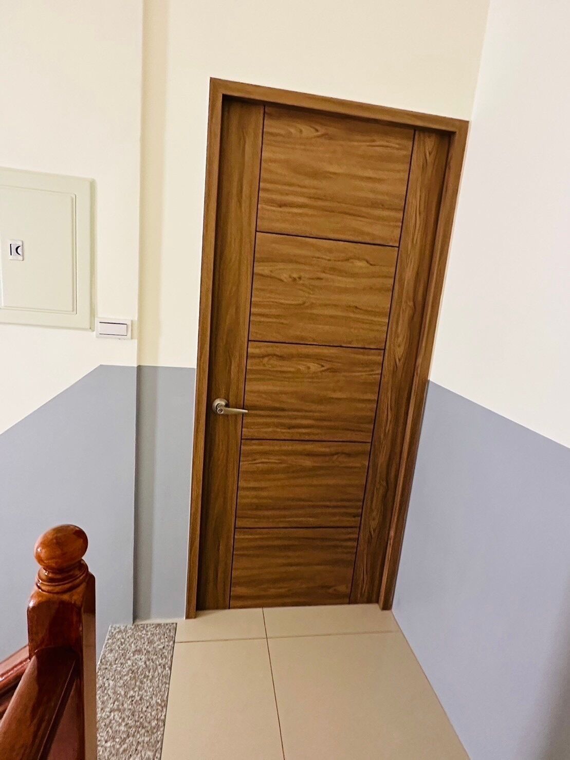 A wooden door with a metal handle, a light switch, and a small wooden object on the floor.