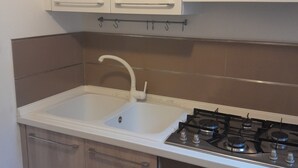 A kitchen with white cabinets, a double sink, a gas stove, and an oven. - Three-room apartment within walking distance from the sea (Sardegna)