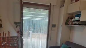 A living room with a patterned floor, a sofa with green cushions, a staircase with a railing, and a door leading to an outdoor area. - Three-room apartment within walking distance from the sea (Sardegna)