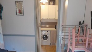A compact living space with a washing machine, a dining table with chairs, and a sofa. - Three-room apartment within walking distance from the sea (Sardegna)