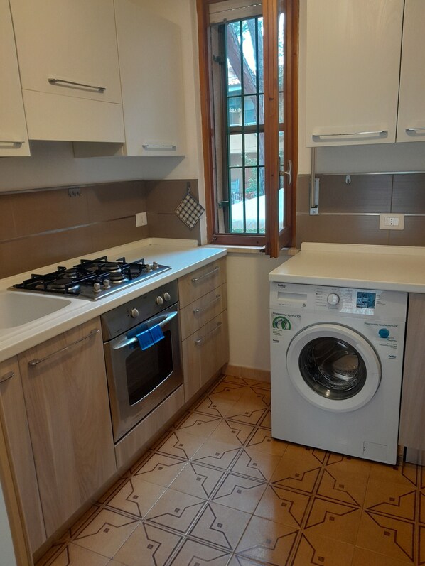 Een kleine keuken met een gasfornuis, oven en een voorlader wasmachine.