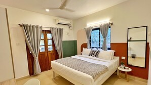 A bedroom with a bed, a bedside table, a chair, a mirror, and an air conditioning unit. - Olive Hotel Calangute Niwasa by Embassy Group (Calangute)