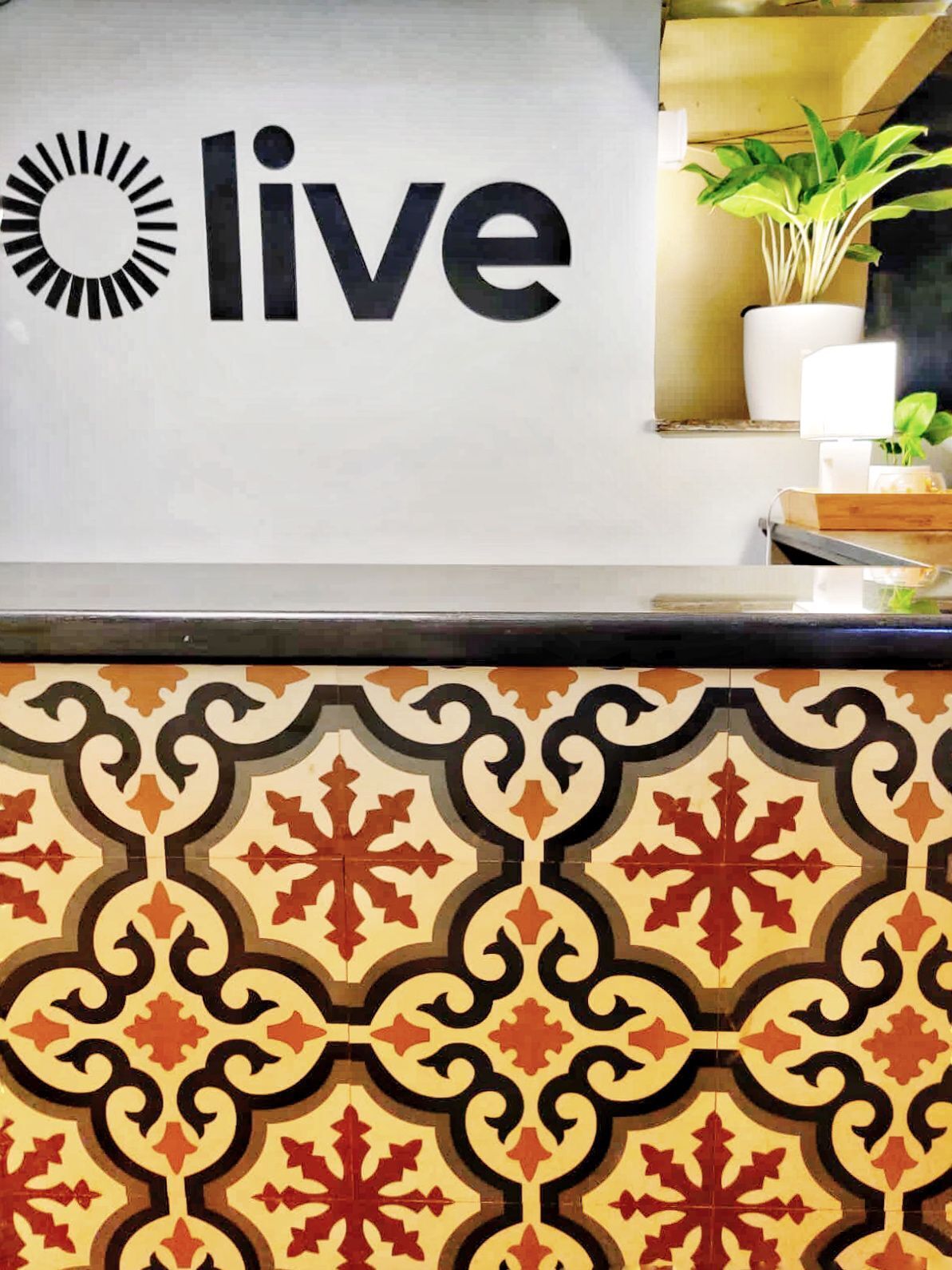 Un comptoir d’accueil avec une pancarte indiquant « service ouvert », un motif décoratif sur le carrelage et une plante en pot.