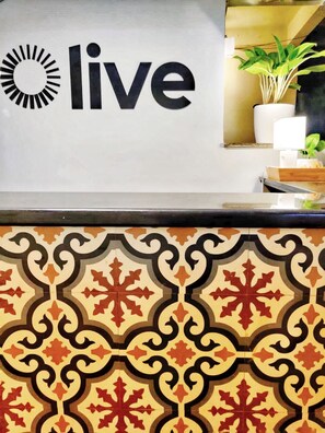 A reception desk with a 'live' sign, a patterned tile design, and a potted plant. - Olive Hotel Calangute Niwasa by Embassy Group (Calangute)