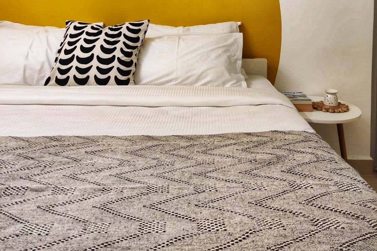 Ein Bett mit einem gemusterten Überwurf, ein weißes Kissen mit einem schwarzen Muster und eine gelbe Akzentwand.
