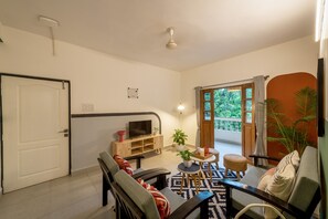 A living room with a sofa, a coffee table, a TV, and a potted plant. - Olive Hotel Calangute Niwasa by Embassy Group (Calangute)