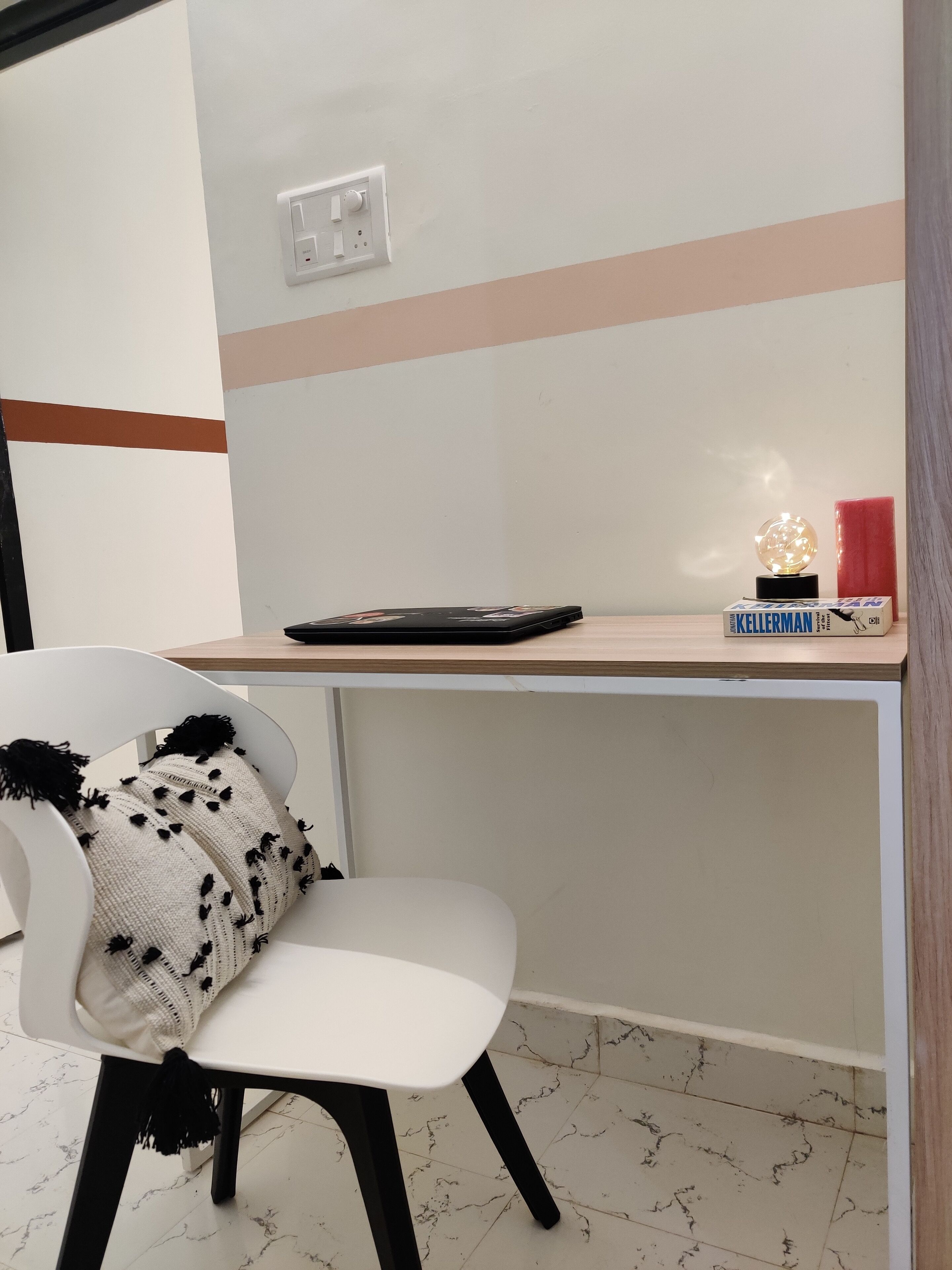 A modern room with a white chair, a small desk, and a red candle.