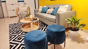 A living room with a grey sofa, blue ottomans, a round coffee table, and a potted plant. - Olive Hotel Calangute Niwasa by Embassy Group (Calangute)