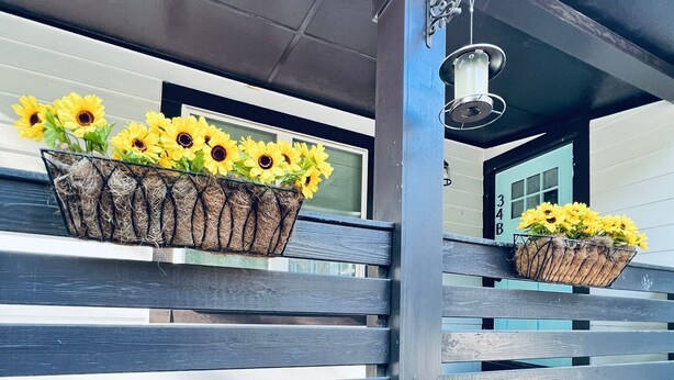 A building with a gray exterior, a wooden fence, and two flower baskets with sunflowers.