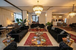 Un vestíbulo amplio con un área de estar central, varios candelabros y un mostrador de recepción.
