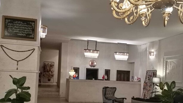 Amplia sala de estar con candelabro, mostrador de recepción y dos plantas en macetas.