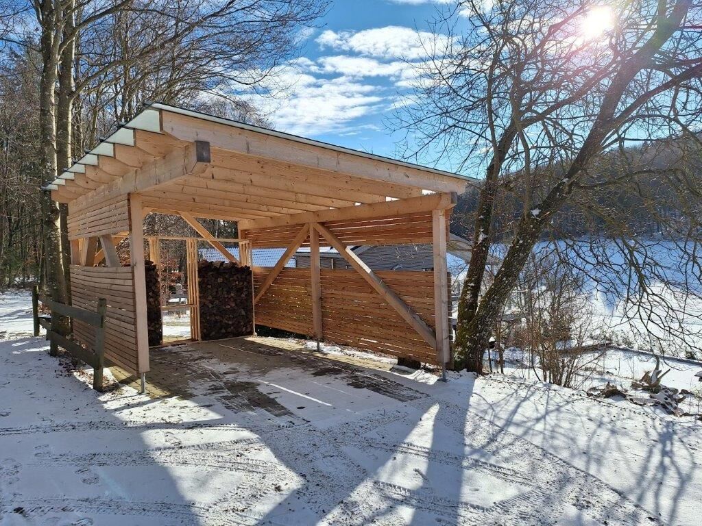 A wooden cabin with a sloped roof, a stone wall, and a wooden door.
