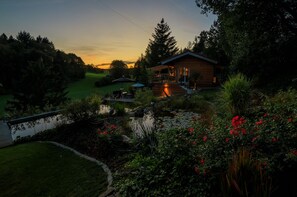 Eine Hütte mit Terrasse, die auf einen Teich und Garten blickt.