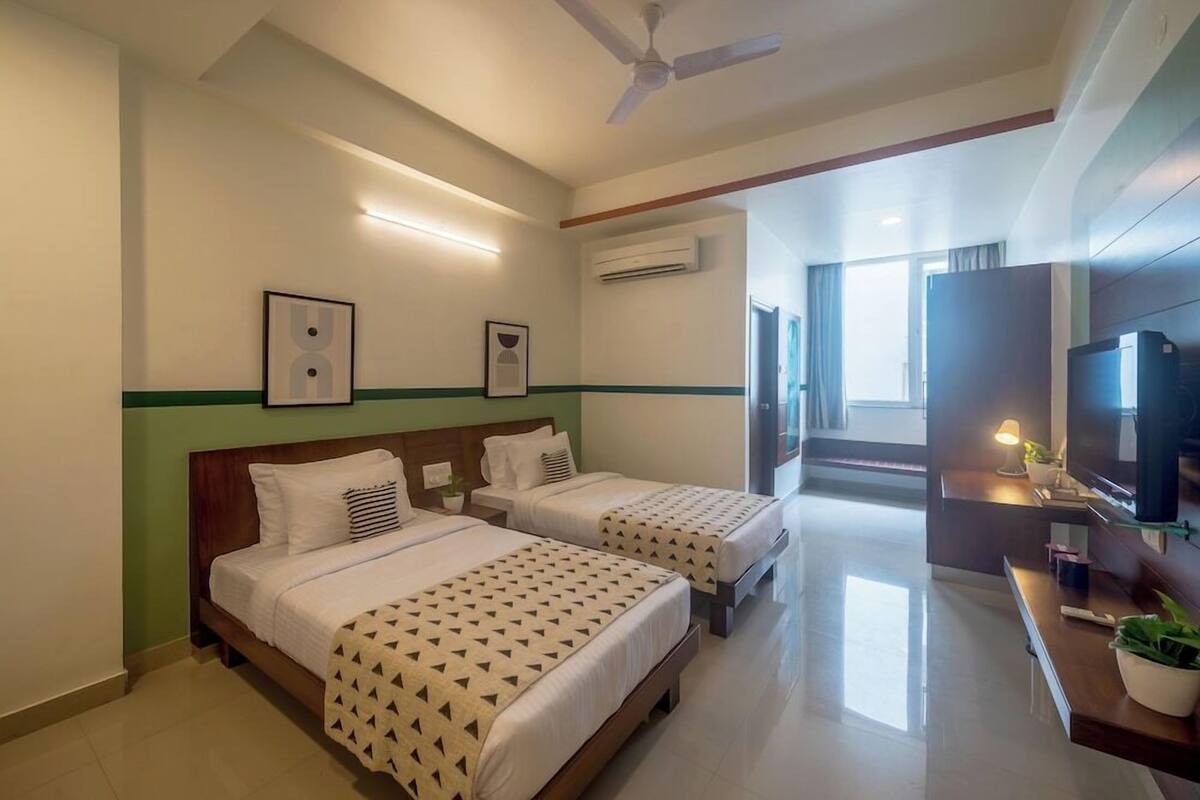 A hotel room with two beds, a ceiling fan, a flat-screen TV, a desk with a lamp, and a potted plant.