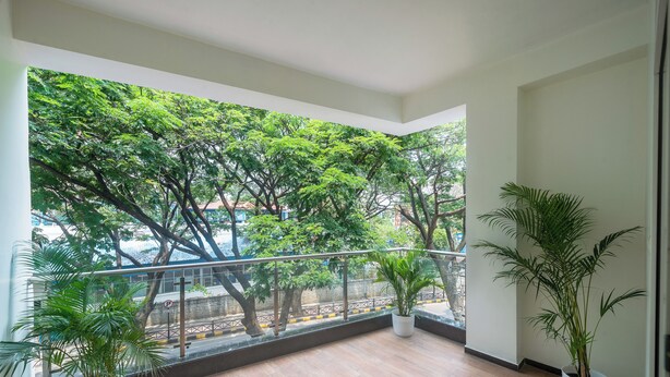 A balcony with a view of trees and a railing. There are potted plants on the balcony floor.
