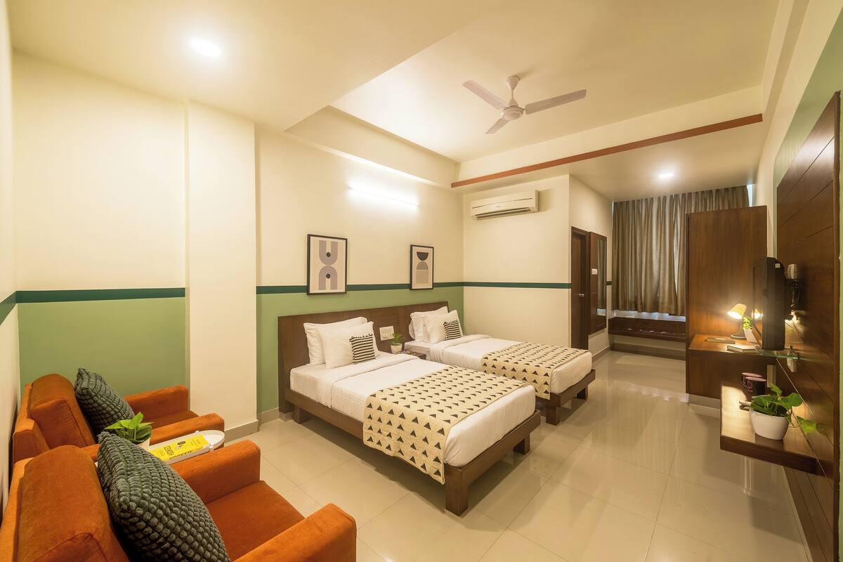 A hotel room with two beds, a sofa, a desk, and a ceiling fan.