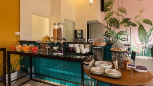 A breakfast buffet with various food items, a coffee machine, and a mural of tropical plants on the wall.