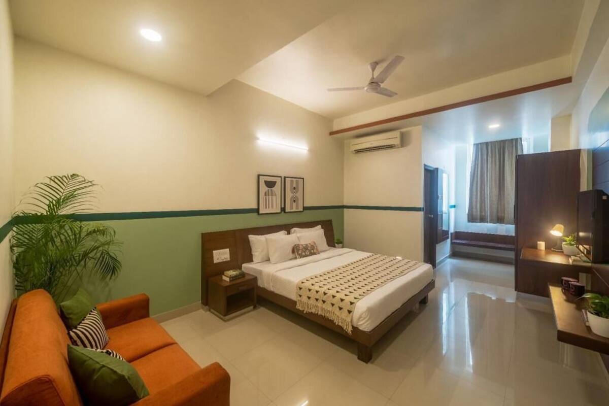 A hotel room with a bed, a nightstand, a sofa, a ceiling fan, and a wall-mounted air conditioner.